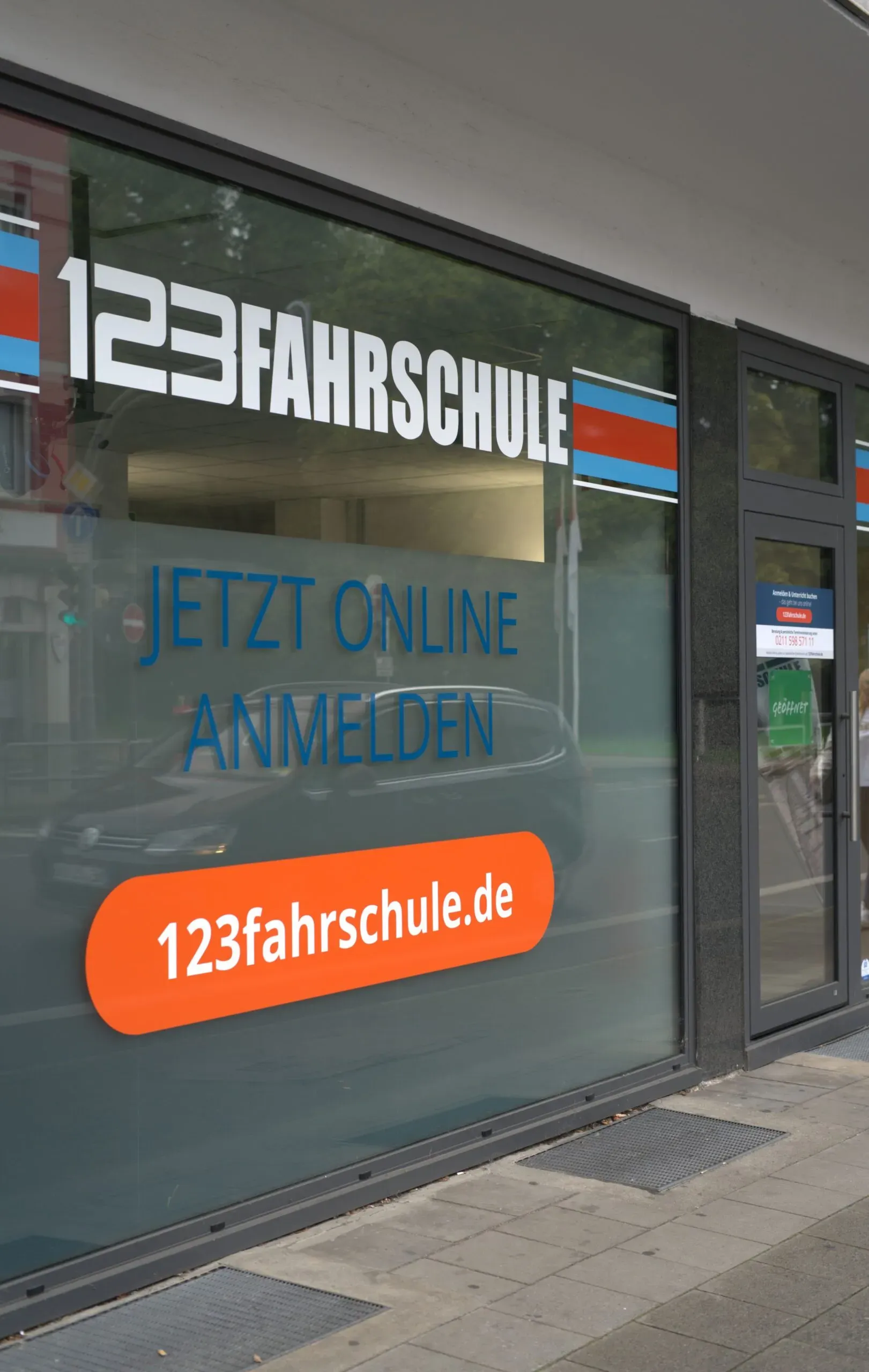 Schaufenster einer Filiale der 123fahrschule mit dem Hinweis „Jetzt online anmelden“