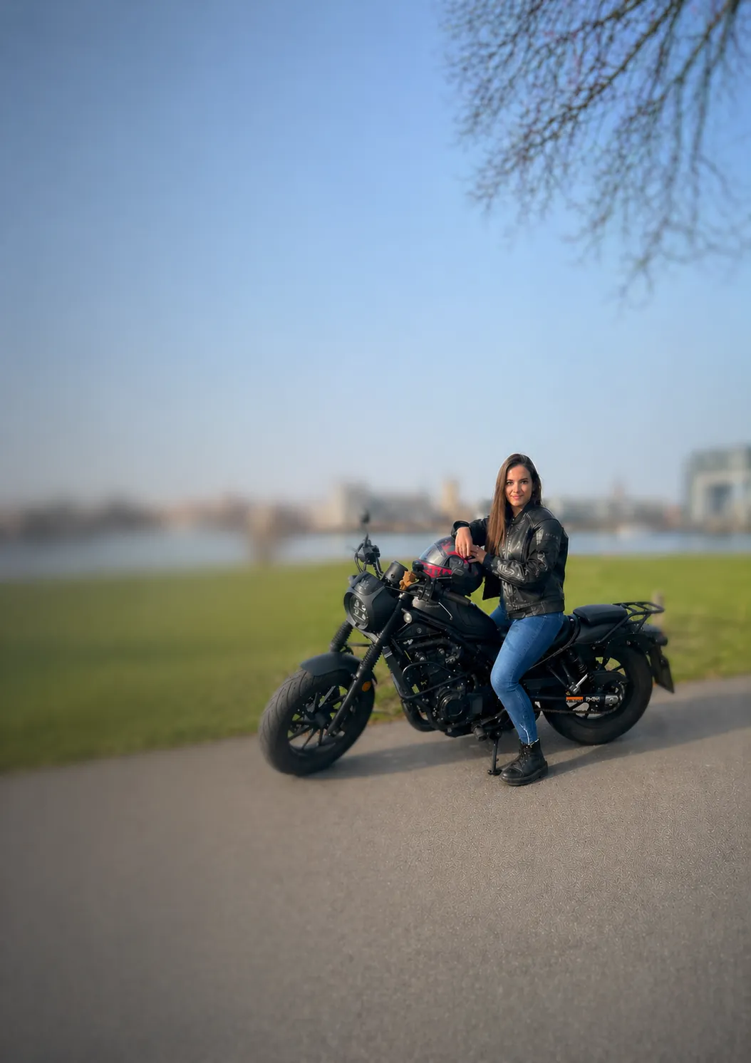 Person in Motorradkleidung mit Helm neben einem Motorrad auf einem Uferweg
